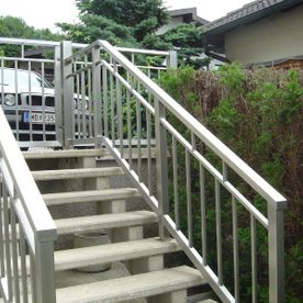Treppe mit Betonstufen und Metallgeländer und Handlauf. Es führt auf eine höhere Ebene, wo im Hintergrund ein KW zu sehen ist.