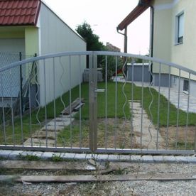 Tor zu einem Grundstück im Rundbogenstil mit modernen gezackten Streben zwischen gerade in unlackiertem Metall